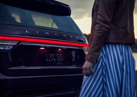 A person is shown near the rear of a 2024 Lincoln Aviator® SUV as the Lincoln Embrace illuminates the rear lights | Griffin Lincoln in Tifton GA