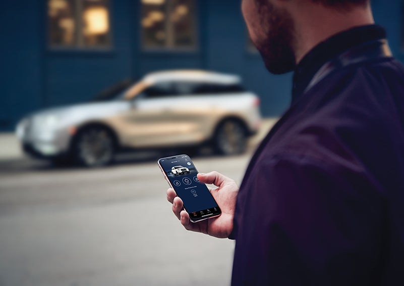 A person is shown interacting with a smartphone to connect to a Lincoln vehicle across the street. | Griffin Lincoln in Tifton GA