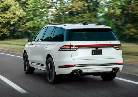 A white 2025 Lincoln Aviator® SUV is being driven away down a road lined with colorful trees. | Griffin Lincoln in Tifton GA