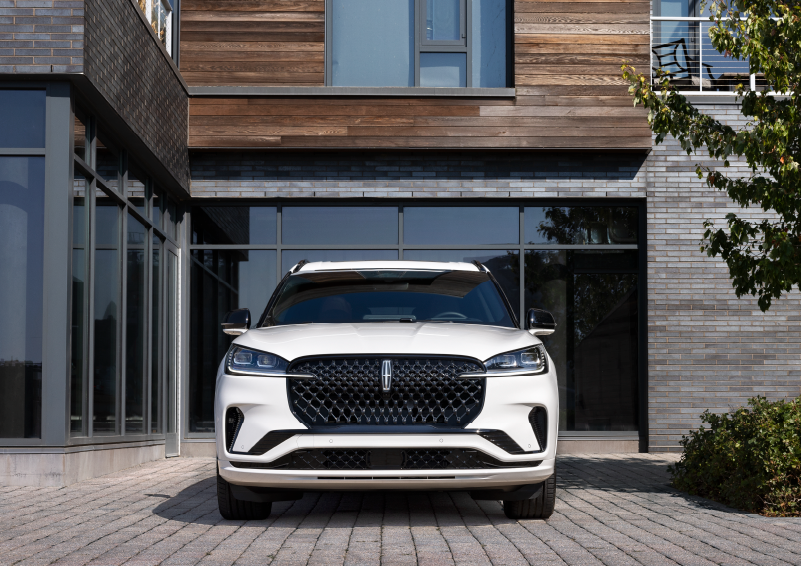 A white 2025 Lincoln Aviator® SUV is shown parked outside a modern building with gray brick and wood accents. | Griffin Lincoln in Tifton GA