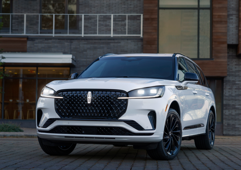A white 2025 Lincoln Aviator® SUV is shown parked outside a modern building with gray brick and wood accents. | Griffin Lincoln in Tifton GA