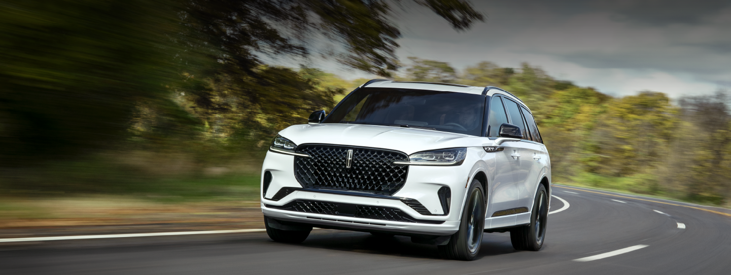 A white 2025 Lincoln Aviator® SUV is being driven down a road lined with trees. | Griffin Lincoln in Tifton GA