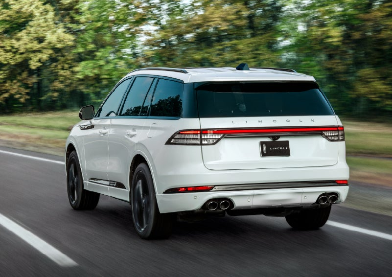 A white 2026 Lincoln Aviator® SUV is being driven away down a road lined with colorful trees. | Griffin Lincoln in Tifton GA