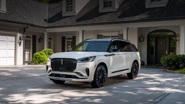A white 2026 Lincoln Aviator® SUV is parked in the driveway of a luxury home. | Griffin Lincoln in Tifton GA