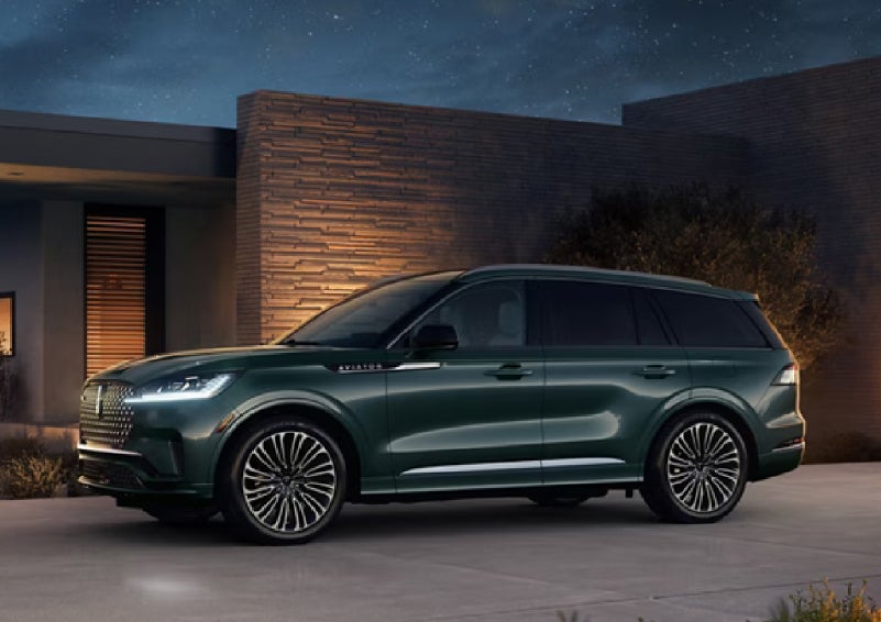 A green 2027 Lincoln Aviator® SUV is parked outside a contemporary home. | Griffin Lincoln in Tifton GA