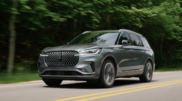 A 2027 Lincoln Aviator® SUV is being driven down a road lined with trees. | Griffin Lincoln in Tifton GA